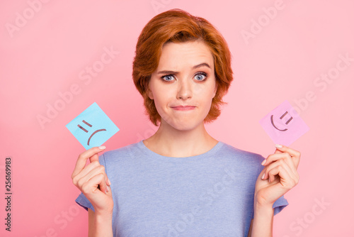 Close-up portrait of her she nice cute charming attractive unsure girl wearing casual blue t-shirt holding in hands two draw notes isolated on pink pastel background photo