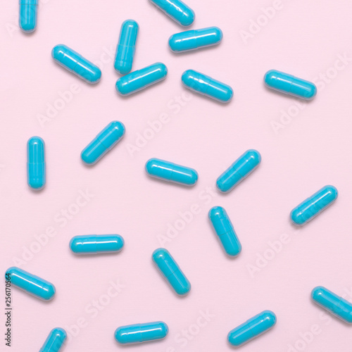 A scattering of blue pills on a pink background, a lot of capsules, top view