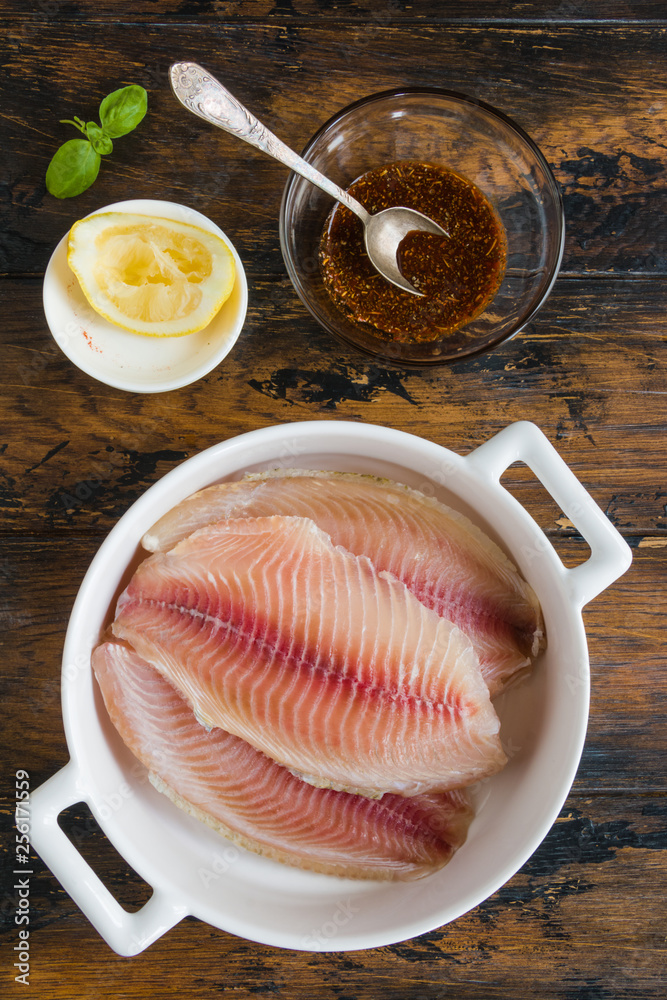 Raw tilapia fish fillet and marinade made from lemon juice, spices and