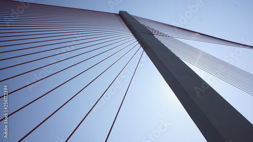 bottom view of a bridge pole with steel cables against a blue sky
