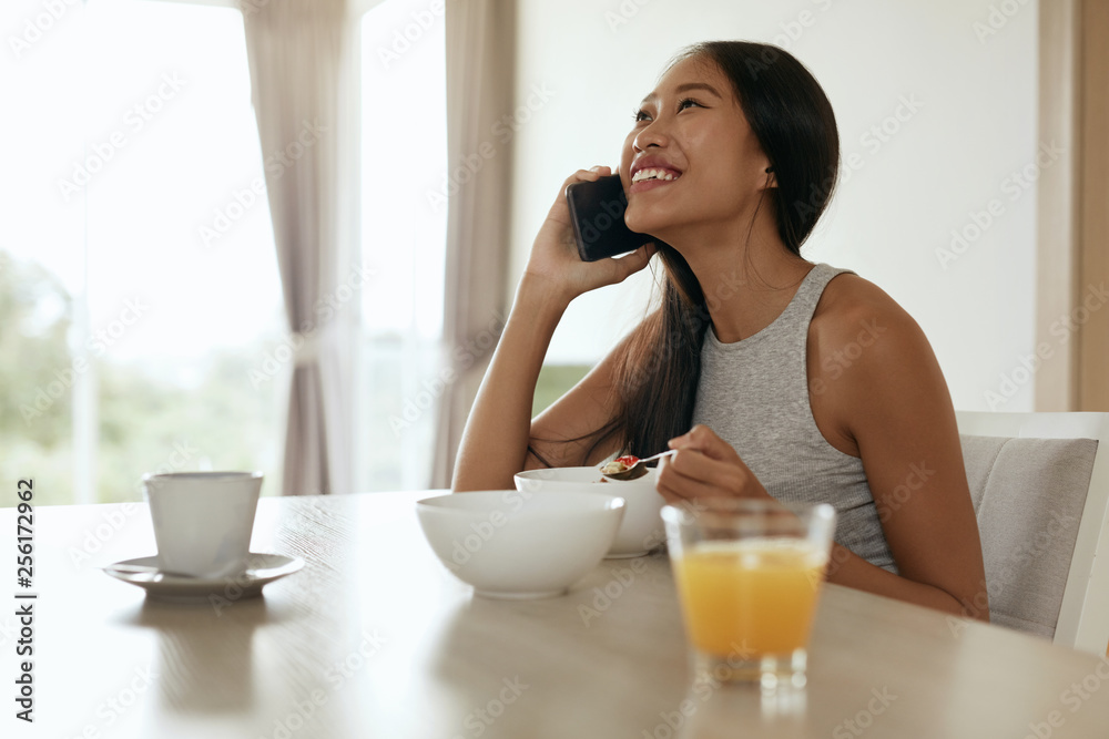 Woman using mobile phone while having breakfast at home