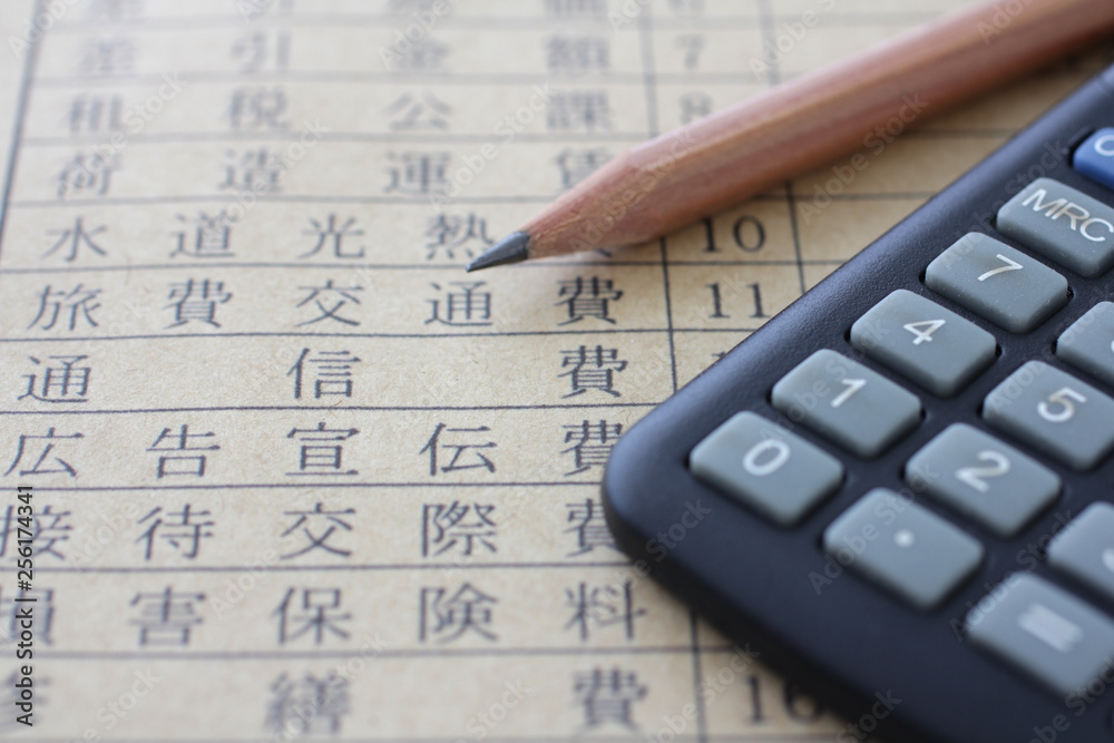 紙に書いた税金や所得や経費と計算機と鉛筆