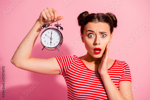 Close-up portrait of her she nice cute charming winsome lovely attractive worried girl wearing striped t-shirt holding showing clock oops omg isolated over pink pastel background