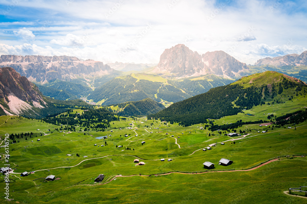 peaceful view of a green valley full of wooden chalet and dolomites mountains over the horizon during summer in val gardena, saslong, south tyrol