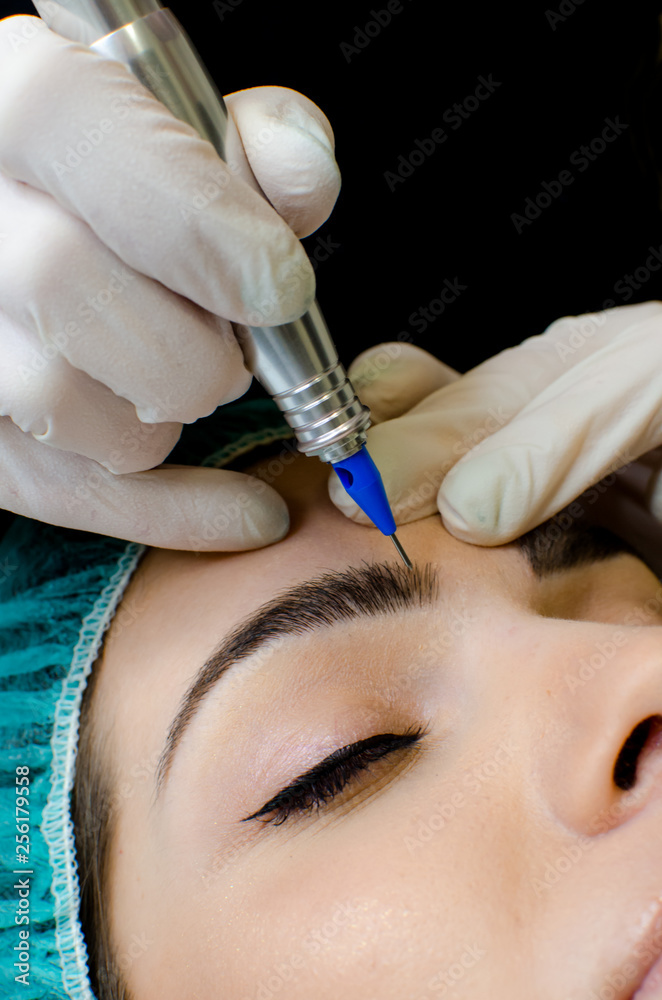 Permanent make-up tattoo, beautician making permanent make up on eyebrows, tattoo procedure on young woman in beauty salon, close up