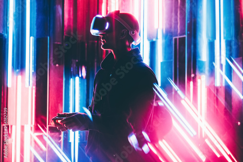 Man using VR headset in dark interior illuminated neon light. Close-up futuristic googles with colored light.shoting through colored flares and bokeh. photo