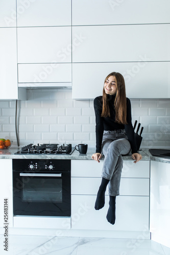 Attractive woman sitting on kitchen counter. Young housewife relaxing in the kitchen.