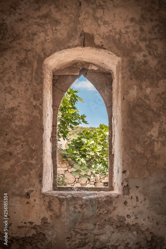 View  at some grean leaves and blue skies through an open window with plastered walls from an old abandoned medieval building in Kato Chora  Kythira  Greece
