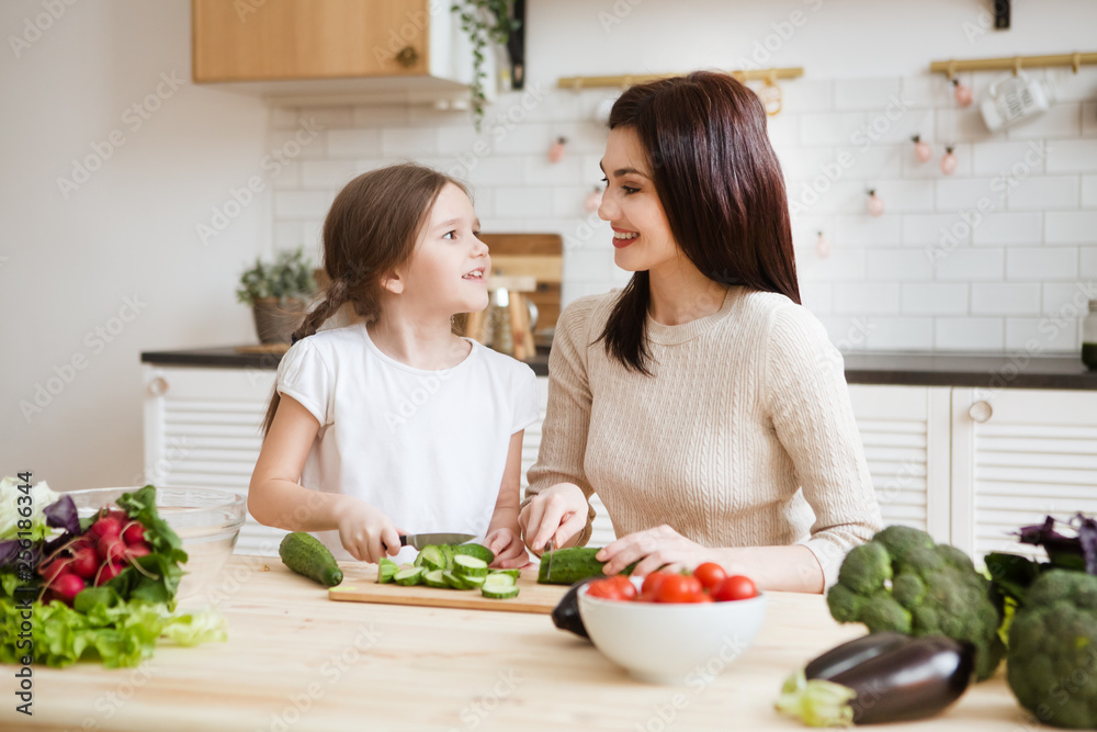 Mother and daughter in preparing healthy vegetables  salad  together  in the kitchen. Help children to parents. 