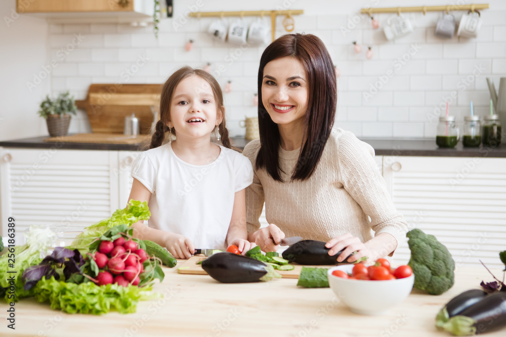 Mother and daughter in preparing healthy vegetables  salad  together  in the kitchen. Help children to parents. 