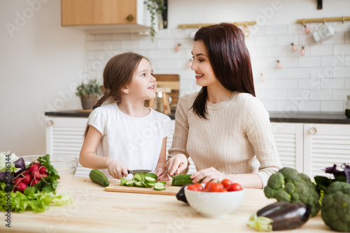 Mother and daughter in preparing healthy vegetables  salad  together  in the kitchen. Help children to parents. 