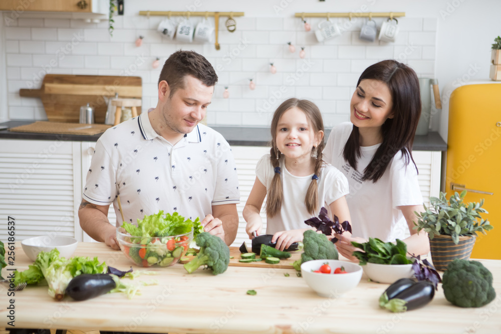 Happy family Mother. father and daughter in preparing healthy vegetables  together  in the kitchen. Help children to parents. 