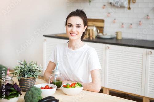 Smiling young woman drinking green smoothie juice in kitchen. Healthy Lifestyle.