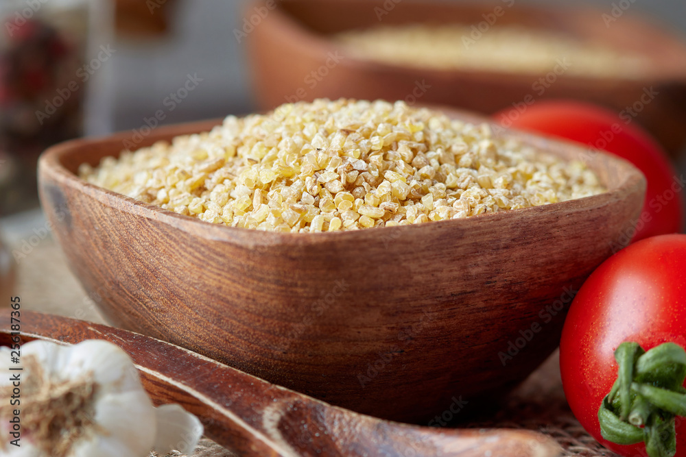 Uncooked raw bulgur wheat grains in wooden bowl Uncooked raw bulgur wheat grains in wooden bowl