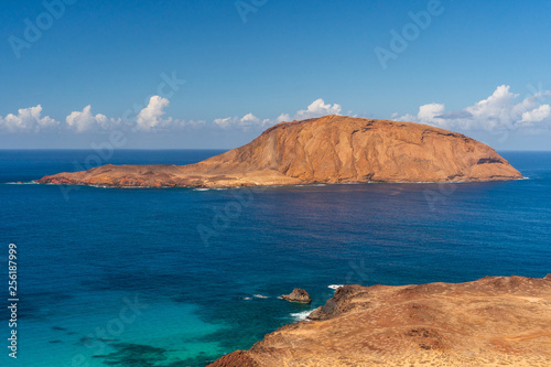 Isla de Montana Clara island as seen from the top of Bermeja volcanic mountain on La Graciosa Island in Lanzarote, Spain. Atlantic Ocean seascape on a warm sunny day under a clear blue sky.