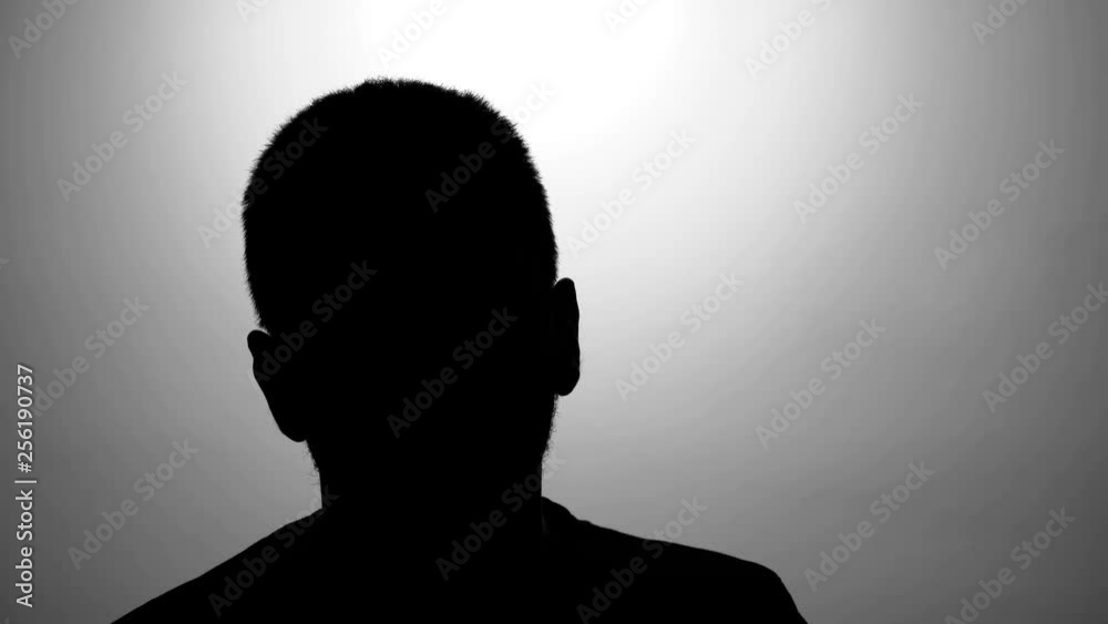 Young caucasian men black silhouette against grey wall talking during interview, hidden identity. Secret testimony of crown witness. The seizure victim answers questions.