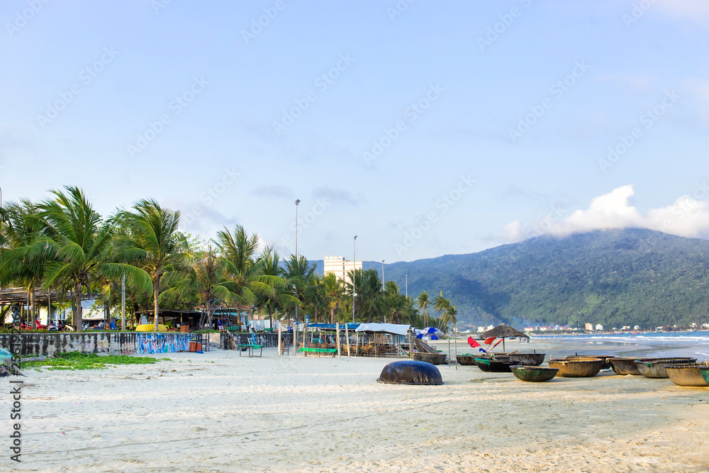 Coconut palm trees at the beach, DaNang, Vietnam. Blue fishing boats at the send. Colorful horizontal image.