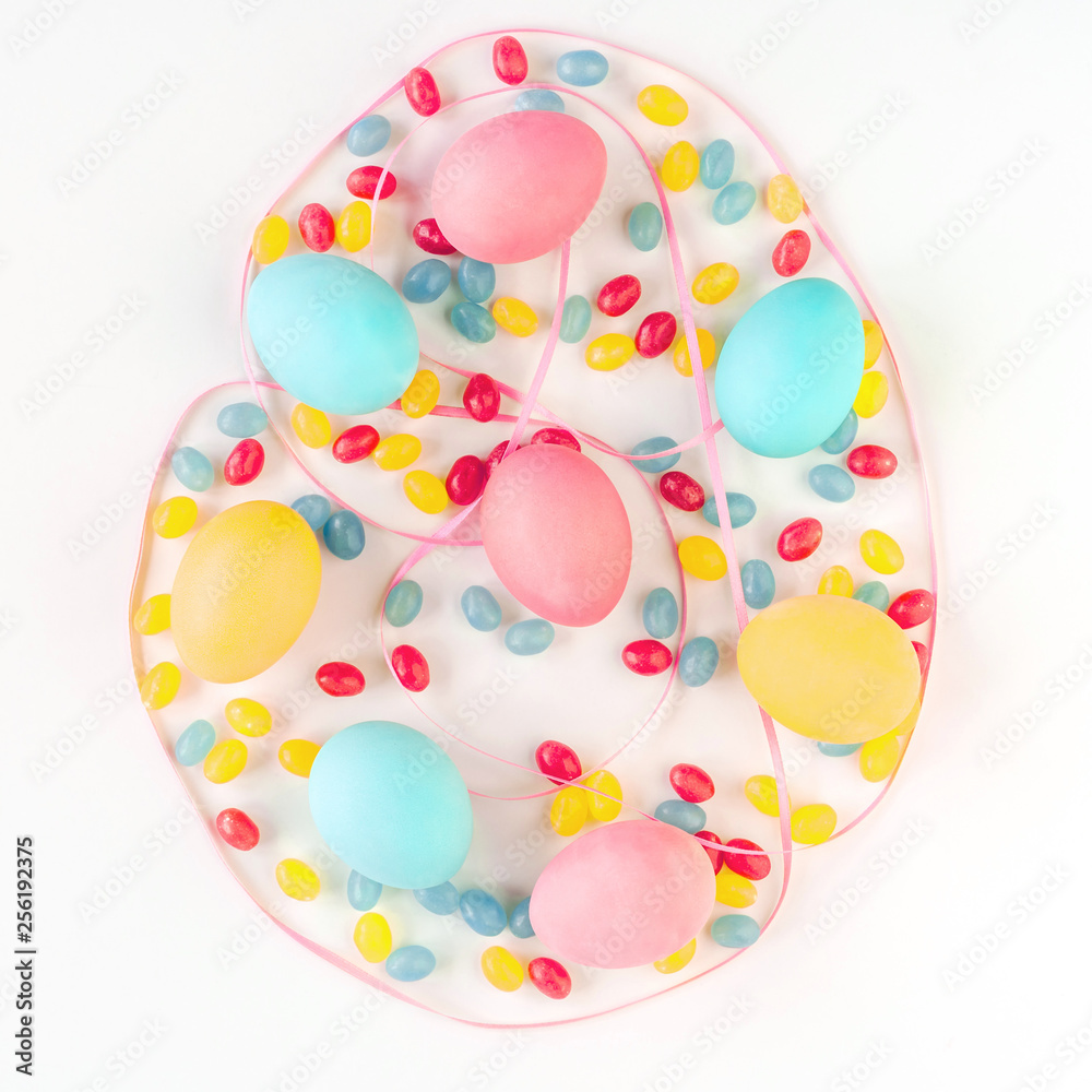 Colorful Easter egg concept. Easter eggs and candies with pink satin ribbon on isolated white background. Flat lay.