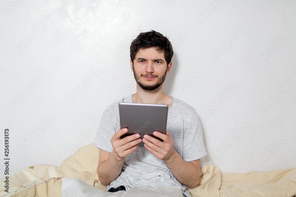 Young man is in bed with a tablet in his hands. White background