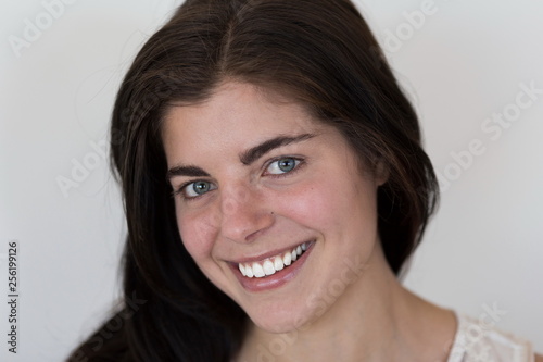 Horizontal closeup of smiling beautiful young brunette girl with piercing green eyes and perfect teeth 