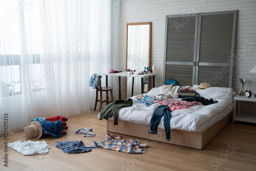 modern bright bedroom with messy clothes scatter on white bed and floor. empty room with nobody in cozy apartment. packing luggage suitcase for summer vacation and spring holidays concept lifestyle. photo