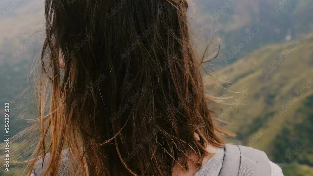 Close-up camera moves round young relaxed woman with backpack enjoying wind blowing in hair at epic mountain scenery. Close-up camera moves round young relaxed woman with backpack enjoying wind blowing in hair at epic mountain scenery.