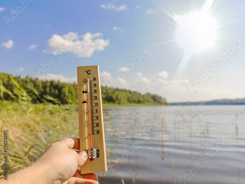 Thermometer showing 30 degrees Celsius of heat against the background of the lake water and the blue sky in sunlight photo