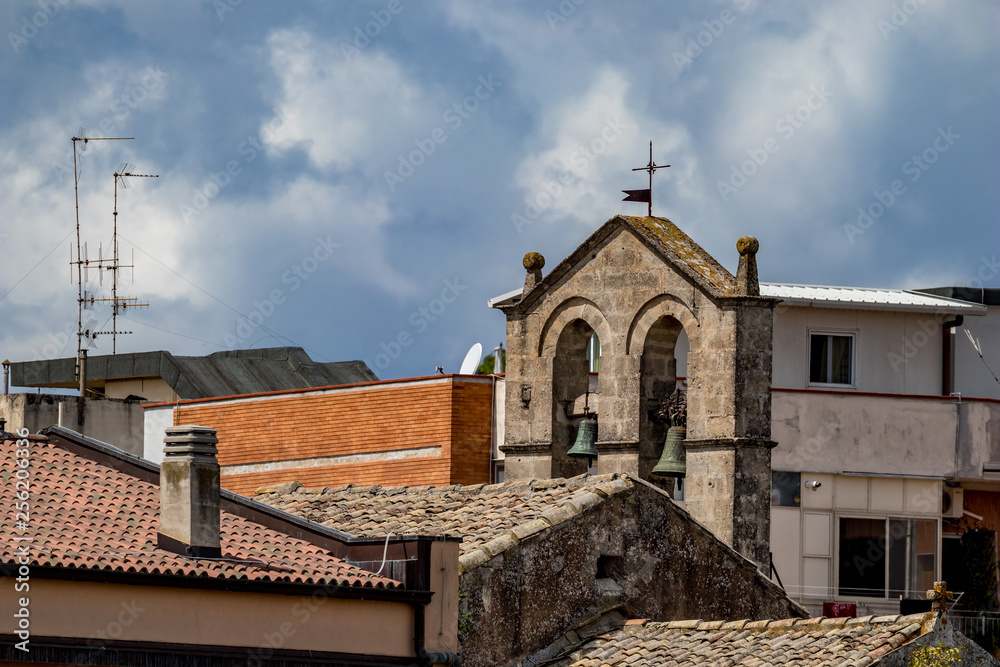Church tower with two brass bells and roof with religious cross, street view of ancient town of Matera, Basilicata, Southern Italy, cloudy summer warm August day