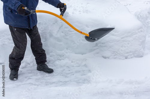 A man cleans snow in the yard with a shovel after a heavy snowfall