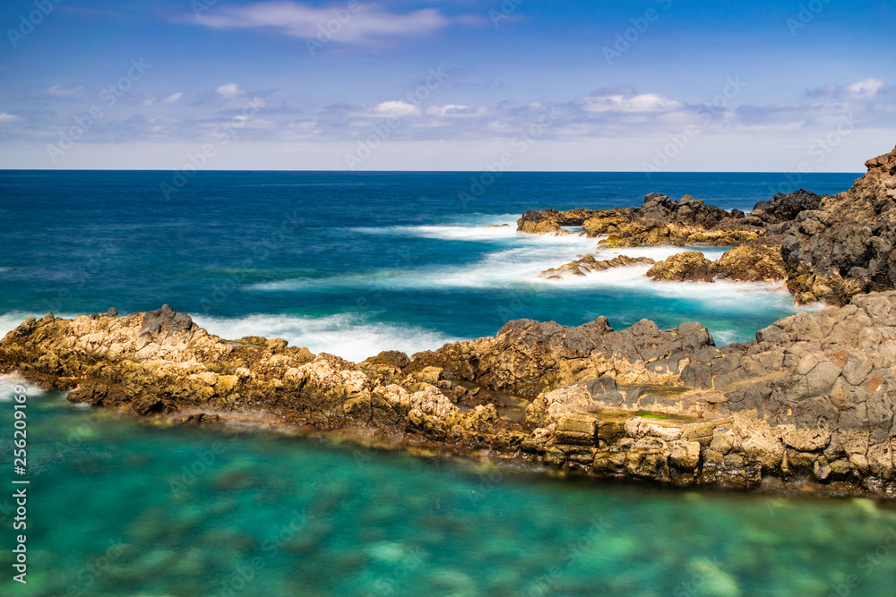 El Sauzal volcanic coastline, long exposure photography, with afternoon sunlight, blue ocean, horizon and blue sky, with few small clouds, Tenerife, Canary islands, Spain