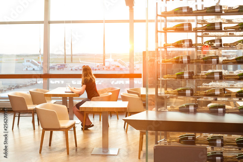 Woman waiting in the cafe in airport terminal and looking at window at airplane