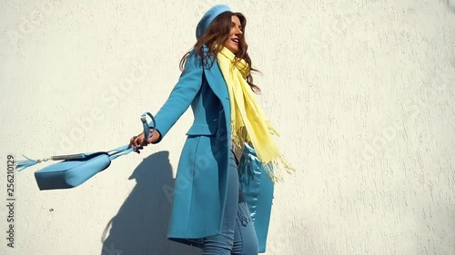 woman posing in a coat on the background of the wall with the handbag
