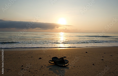 Shoes slippers flip-flops on the beach. Shoes on the sand by the sea on holiday. Shoes with sunrise background 