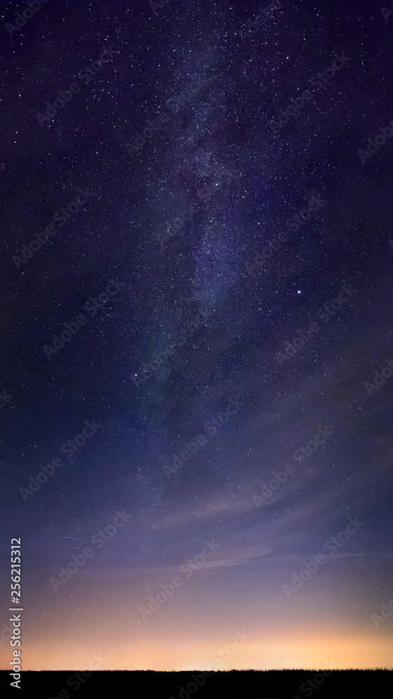 A beautiful milky way with bright stars over flat land at midnight. Night landscape with orange town lights.