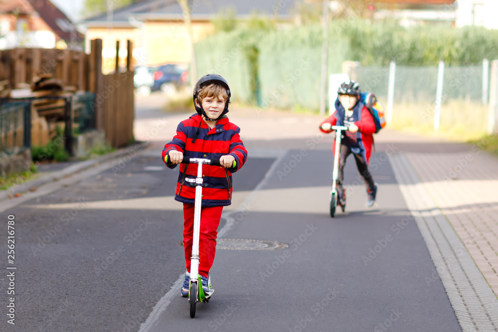 Two little kids boys riding on push scooters on the way to or from school. Schoolboys of 7 years driving through rain puddle. Funny siblings and best friends playing together. Children after school Two little kids boys riding on push scooters on the way to or from school. Schoolboys of 7 years driving through rain puddle. Funny siblings and best friends playing together. Children after school