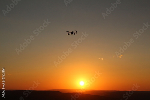 Modern technology showing a silhouetted drone flying against an orange sunset background.