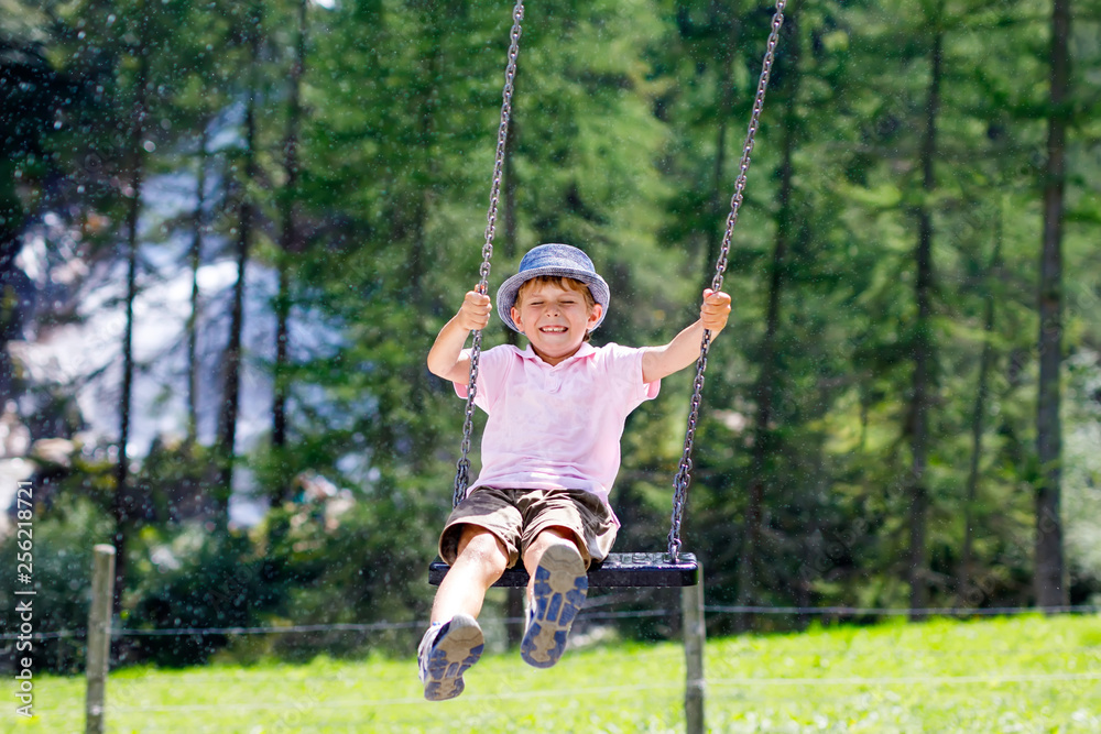 Funny kid boy having fun with chain swing on outdoor playground while being wet splashed with water. child swinging on summer day. Active leisure with kids. Happy crying boy with rain drops on face.