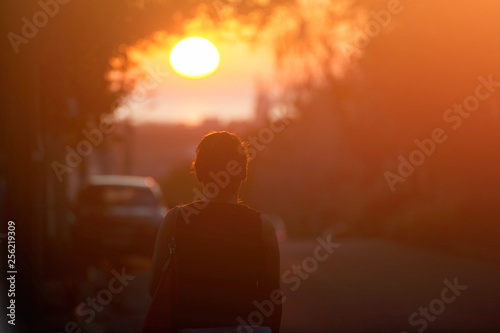 silhouette of adult woman walking alone along city street during beautiful warm sunset