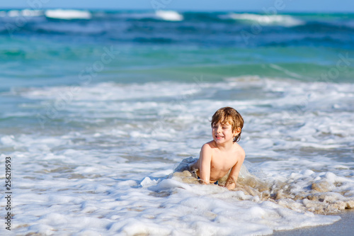 Adorable little blond kid boy having fun on ocean beach. Excited child playing with waves, swimming, splashing and happy about family vacations in Miami, Florida, USA. © Irina Schmidt