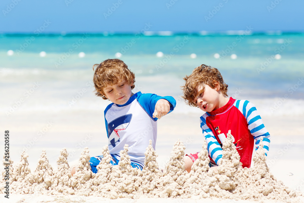 Two little kids boys having fun with building a sand castle on tropical beach of carribean island. children playing together on their vacations Twins, Happy brothers laughing and smiling. Two little kids boys having fun with building a sand castle on tropical beach of carribean island. children playing together on their vacations Twins, Happy brothers laughing and smiling.