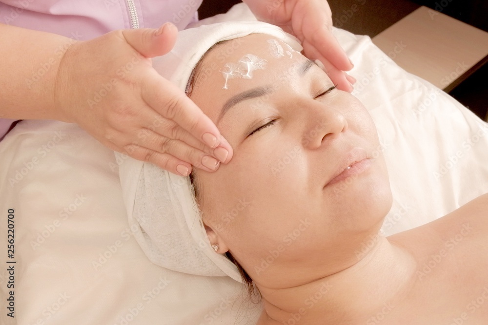 The girl takes a massage procedure in the beauty salon. Female hands do massage of the temples on the girl's head. Beauty. face care. Beautician rubs cream on the face of the girl. The girl takes a massage procedure in the beauty salon. Female hands do massage of the temples on the girl's head. Beauty. face care. Beautician rubs cream on the face of the girl.