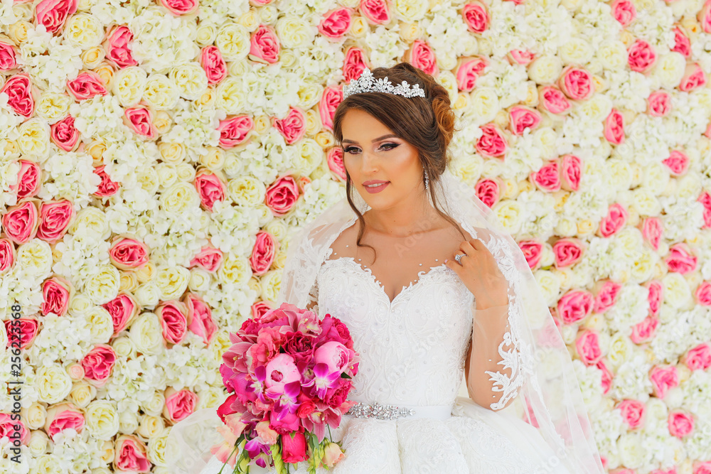 Beautiful fashion bride posing with bouquet of flowers in front of wedding flower wall Beautiful fashion bride posing with bouquet of flowers in front of wedding flower wall