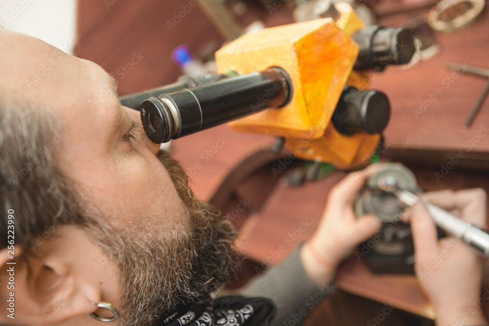 Fototapeta premium Professional craftsman using microscope while repairing jewelry on his vintage workbench