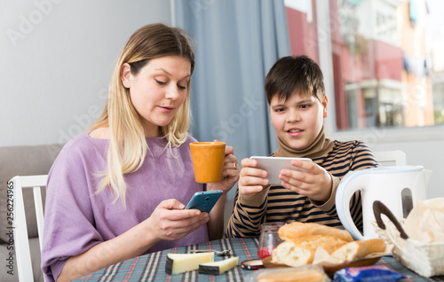 Portrait of young mother and son  using phones during breakfast