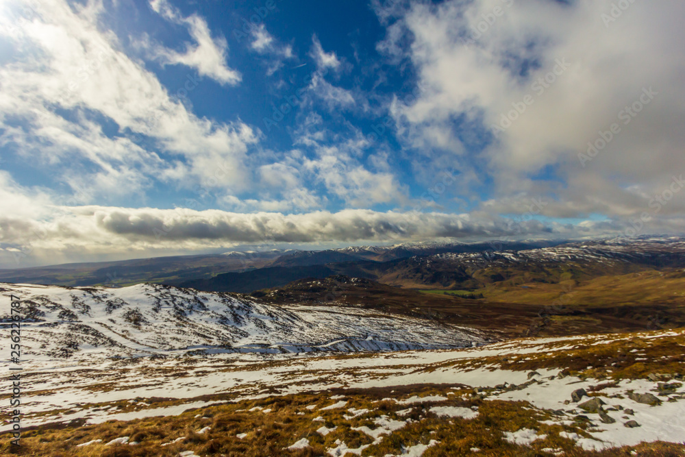 A view of snowy mountain slopes with several other snowy summit in the background under a majestic blue sky and white clouds A view of snowy mountain slopes with several other snowy summit in the background under a majestic blue sky and white clouds