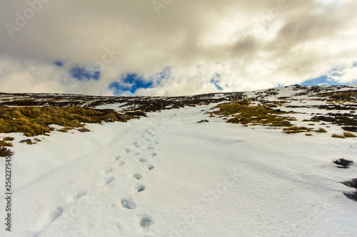 Snow foot traces in the mountain under a majestic blue sky and white clouds