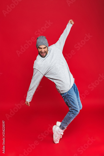 Full length photo of stylish man smiling and jumping isolated over red background