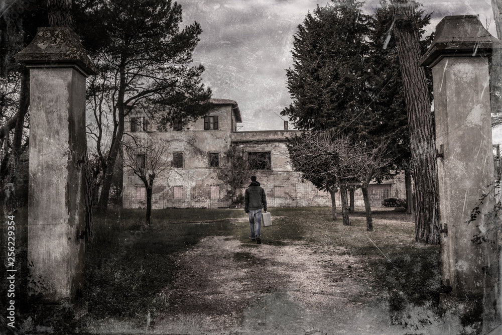 film vintage filter. young man with a suitcase walking in front of a creepy  old abandoned house