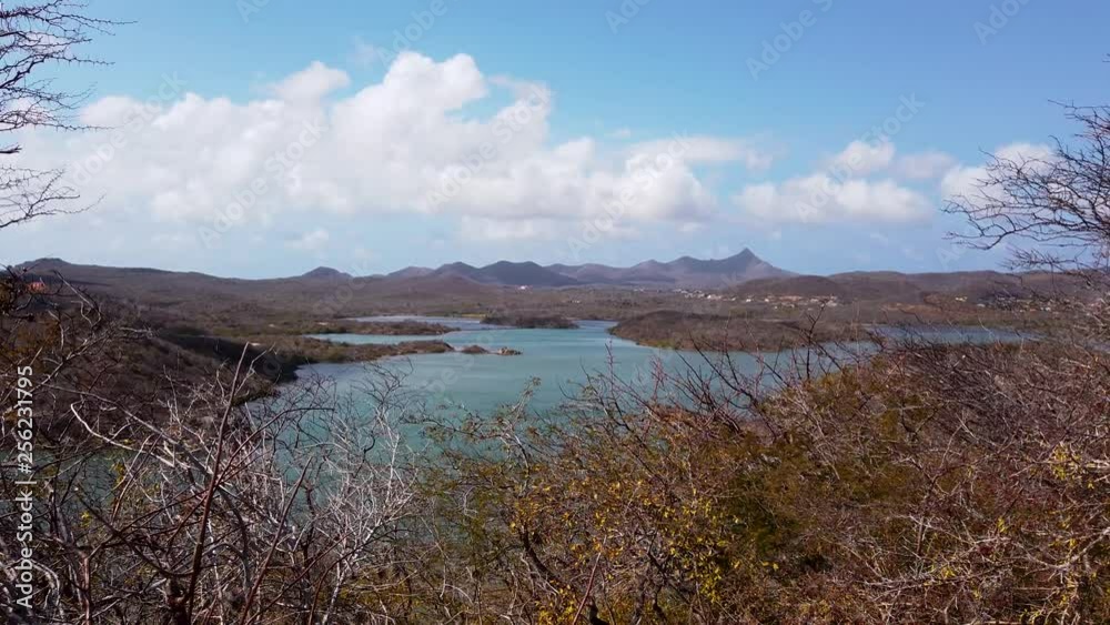 Bay on a Caribbean island, Santa Martha bay on Curacao with mountains in background, naturally framed by shrubs and cloudscape, mountains in background. Bay on a Caribbean island, Santa Martha bay on Curacao with mountains in background, naturally framed by shrubs and cloudscape, mountains in background.