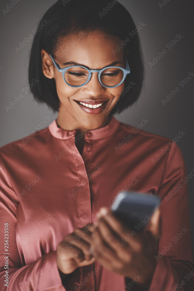 Fototapeta premium Smiling African businesswoman using her cellphone against a gray